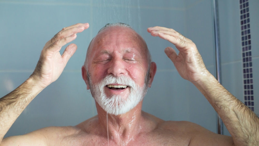 En äldre man står i duschen och ler med rinnande vatten