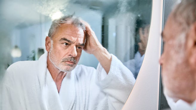 äldre man i badrock tittar eftertänksamt in i immig badrumsspegel