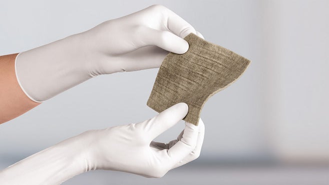 Askina Calgitrol AG+, lätt vågig, hålls av två händer i vita undersökningshandskar