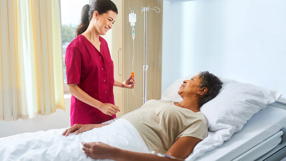 Sjuksköterska med Ecoflac plus på ett infusionsstativ pratar med en sängliggande patient