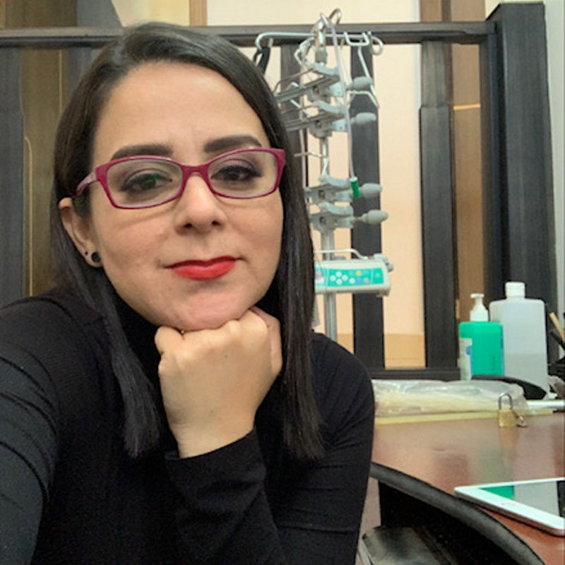 kvinna med mörkt hår, glasögon och läppstift vilar huvudet mot handen