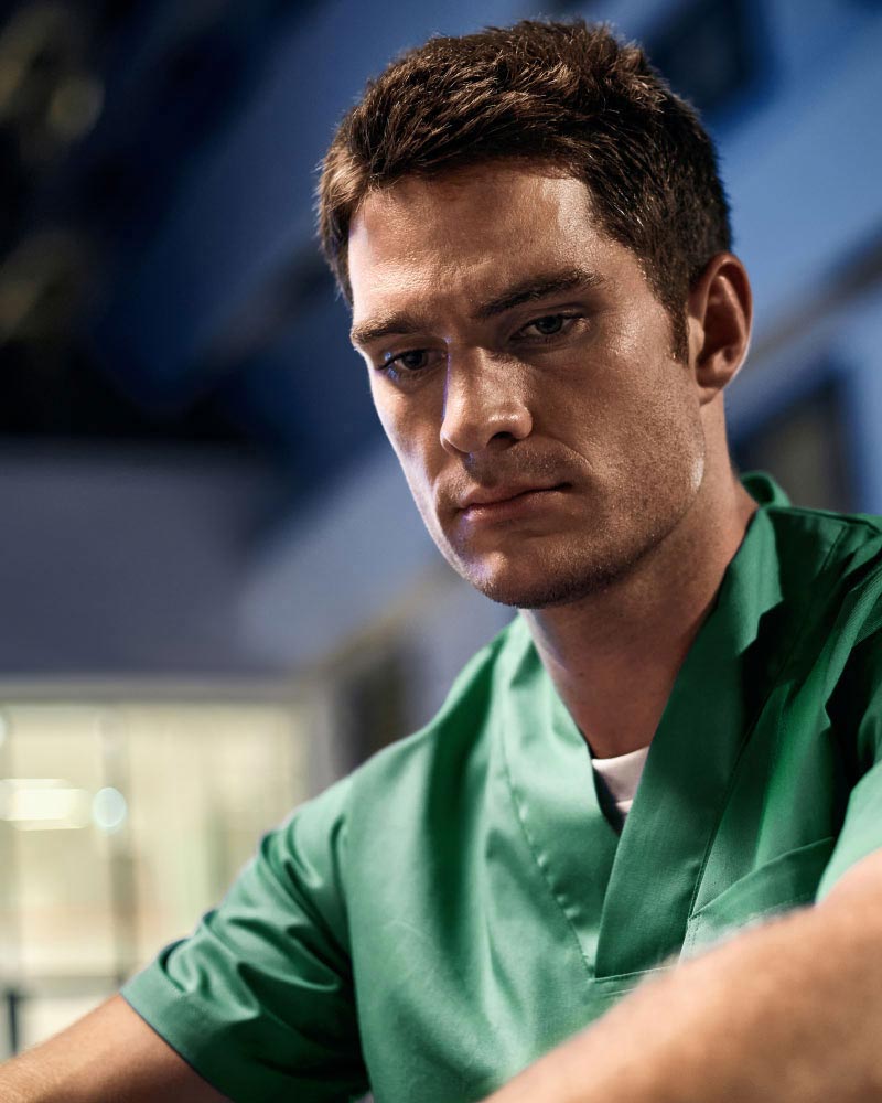 Utmattad sjuksköterska som sitter framför ett sjukhus