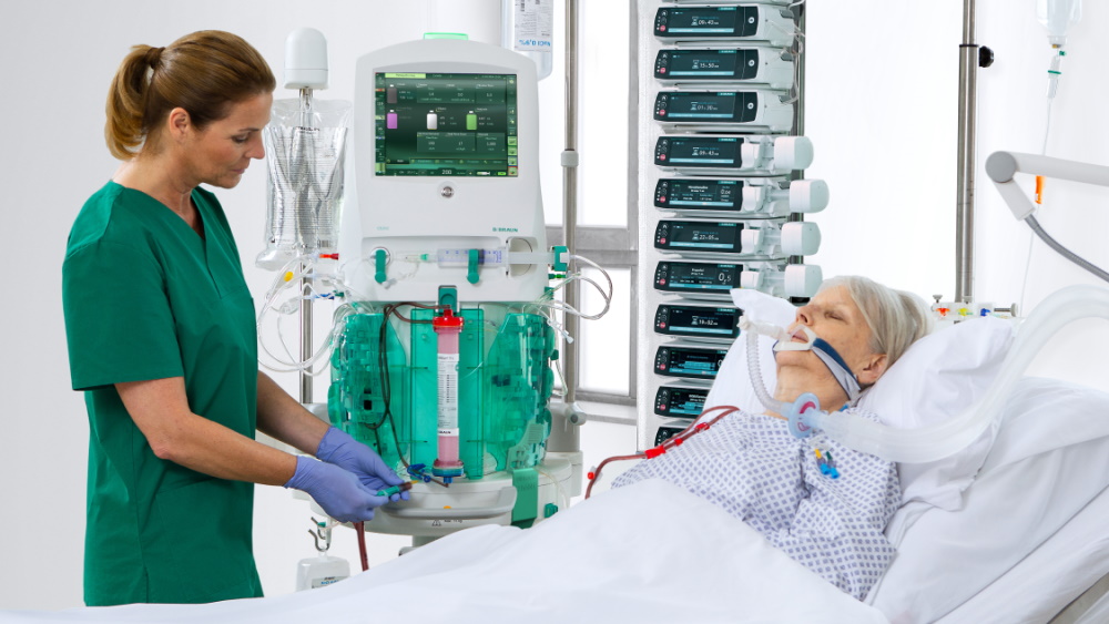 En patient ligger i sängen och är ansluten till dialysmaskinen. Sjuksköterskan använder maskinen.