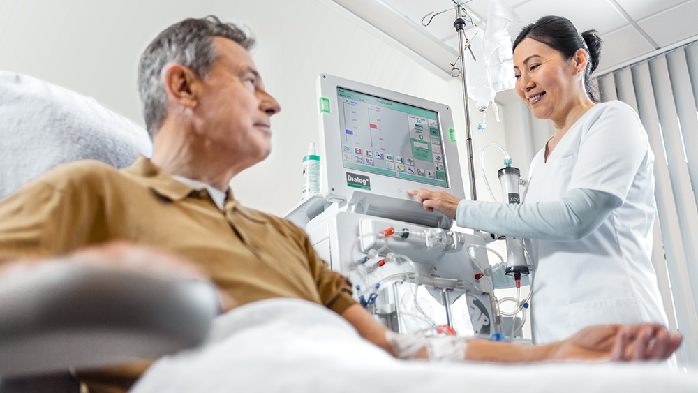 En patient är ansluten till en dialysmaskin. En sjuksköterska står bredvid honom och manövrerar maskinen.