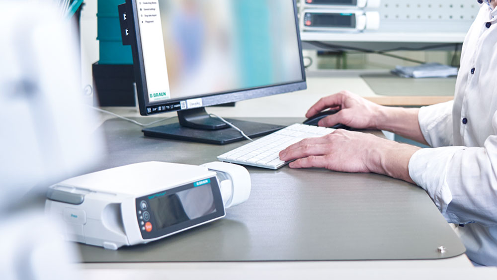 MT Ingengör sitter framför sin dator. I förgrunden finns en infusionspump från B. Braun.