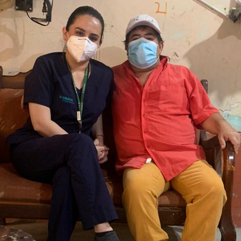 Carol sitter bredvid Carlo i en soffa, båda tittar in i kameran och bär munskydd.