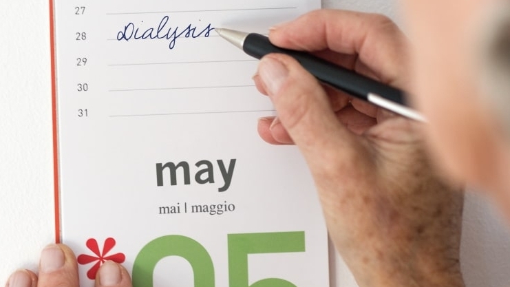 En hand skriver med kulspetspenna in dialys på 28 maj i en kalender