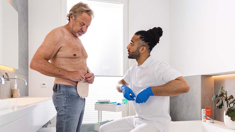 Sjukvårdspersonal visar patient hemma hur man applicerar en B. Braun-stomipåse.