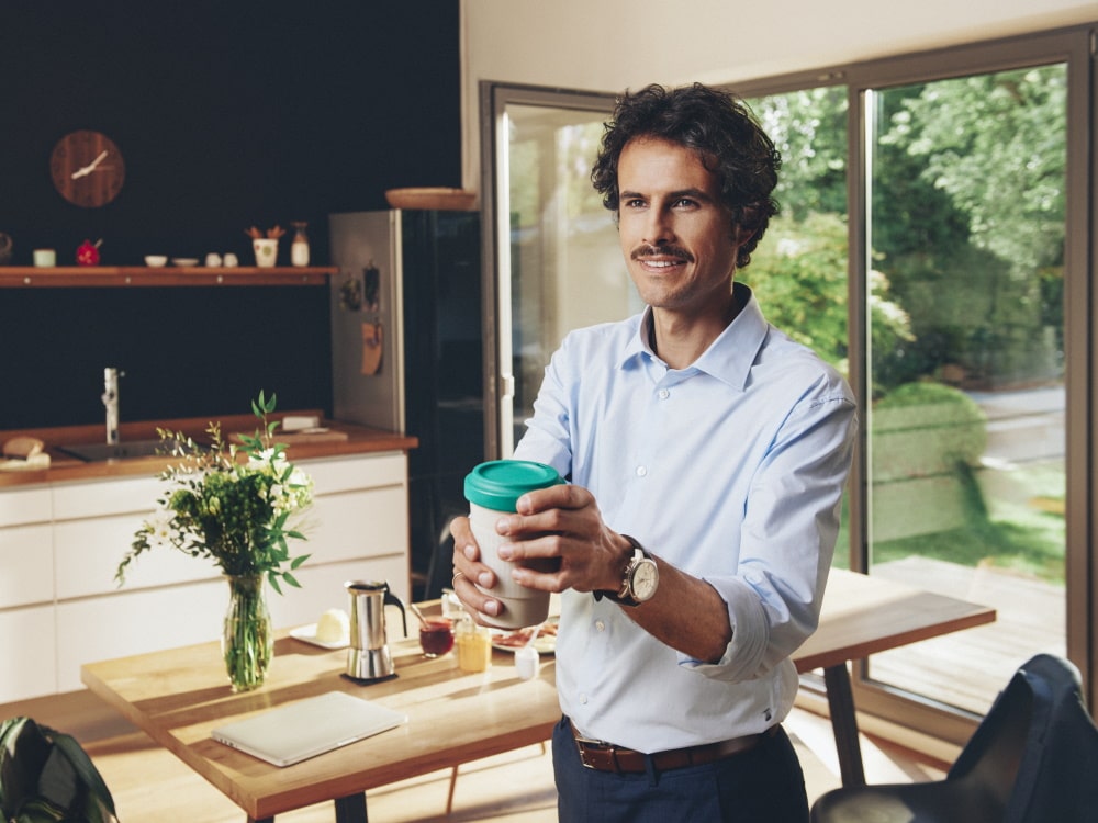 En man står i ett privat hus och håller en kopp kaffe