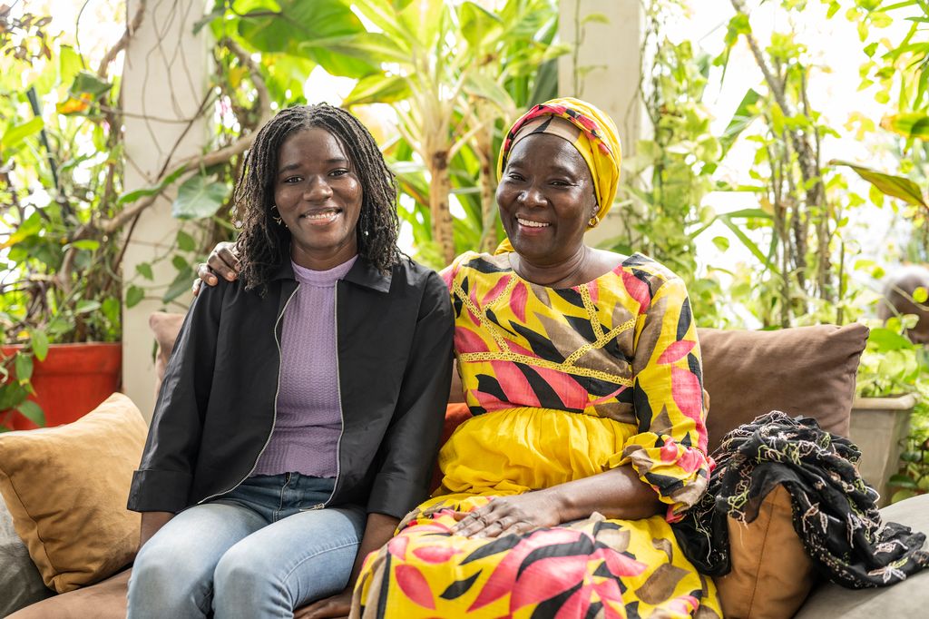 Silberia Diack och hennes mamma sitter på en soffa i ett väl upplyst rum. De håller varandra i sina armar och ler framåt. 